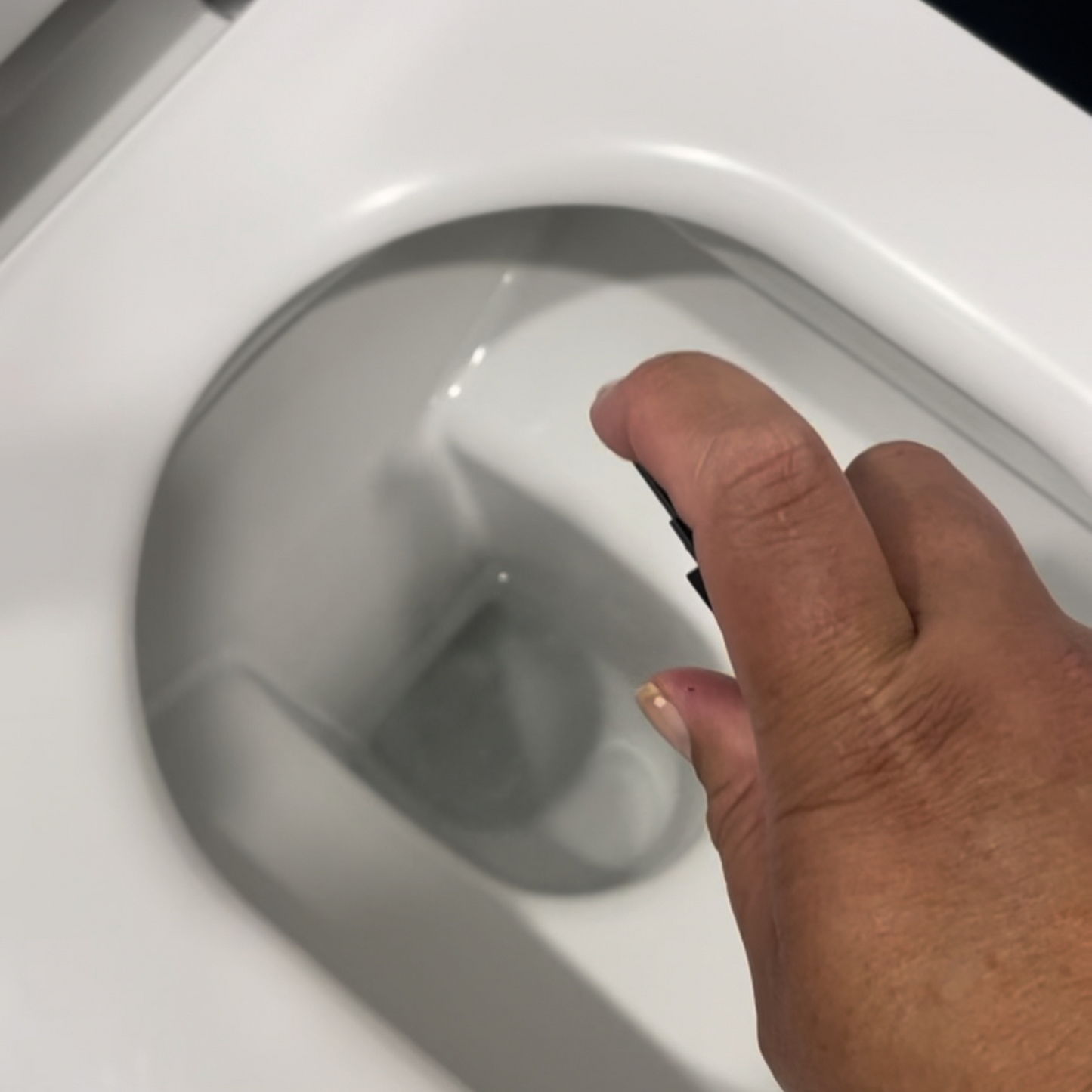 Hand holding bottle of wharepaku deodoriser preparing to spray into the toilet bowl