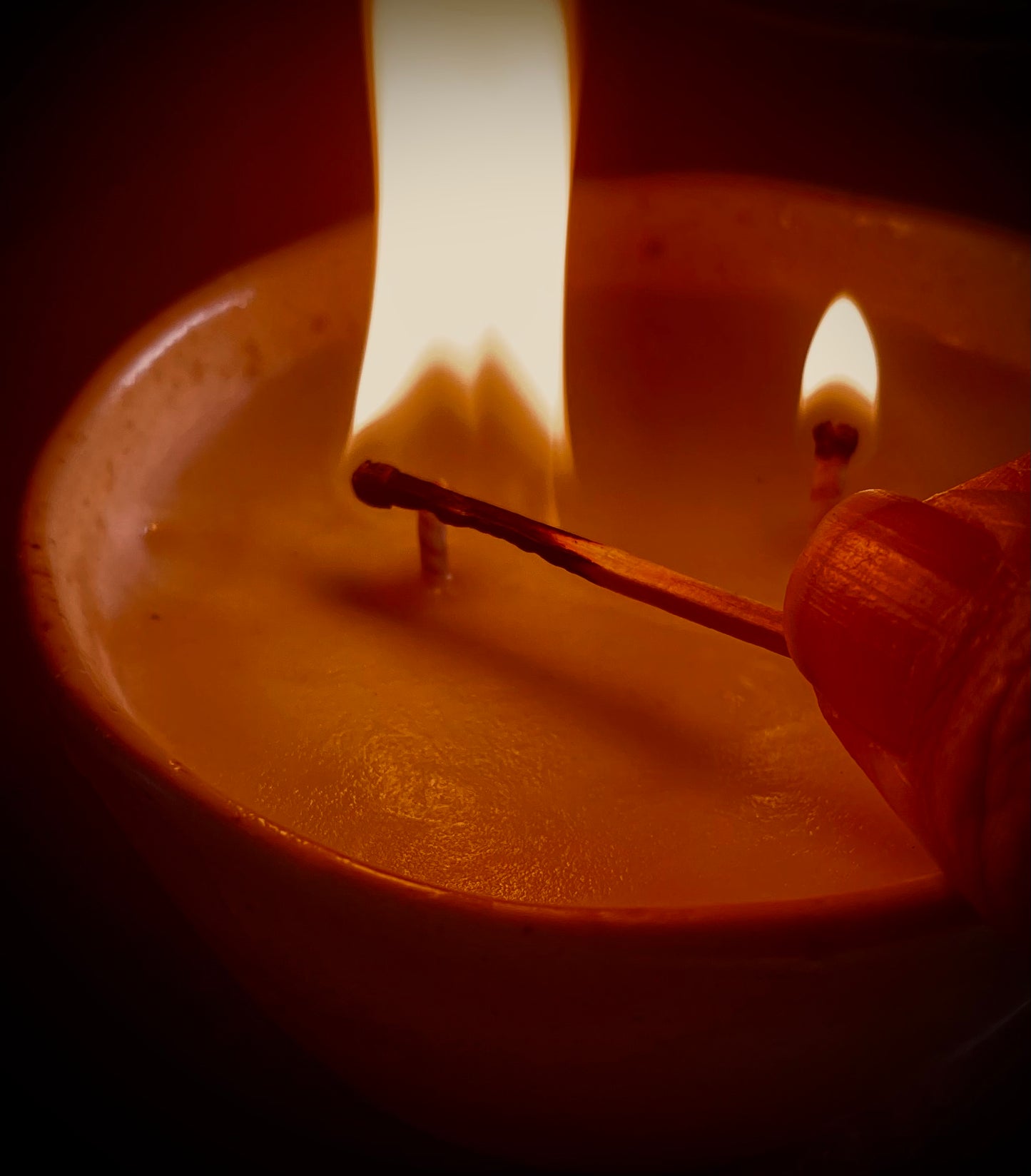 "A ceramic pinch pot holds a body serum candle, radiating a warm glow with its flickering flame."