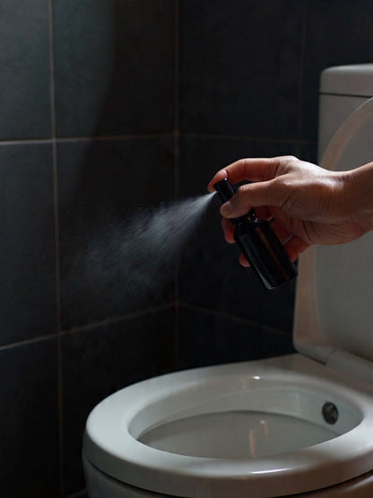 Wharepaku toilet deodoriser in a sleek 30ml black glass bottle being sprayed into a toilet bowl to prevent odours.