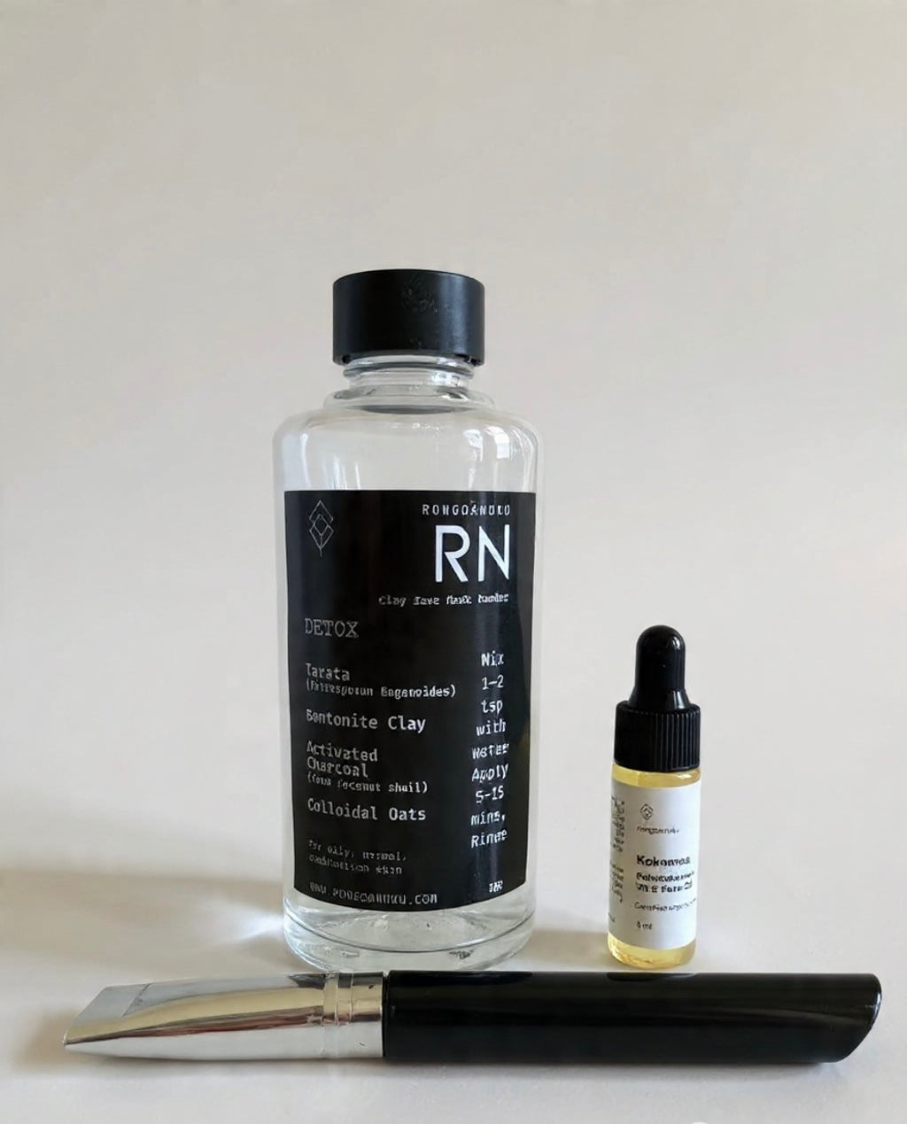 Bottle of Facemask powder with a dropper bottle of face oil and brush on a white background