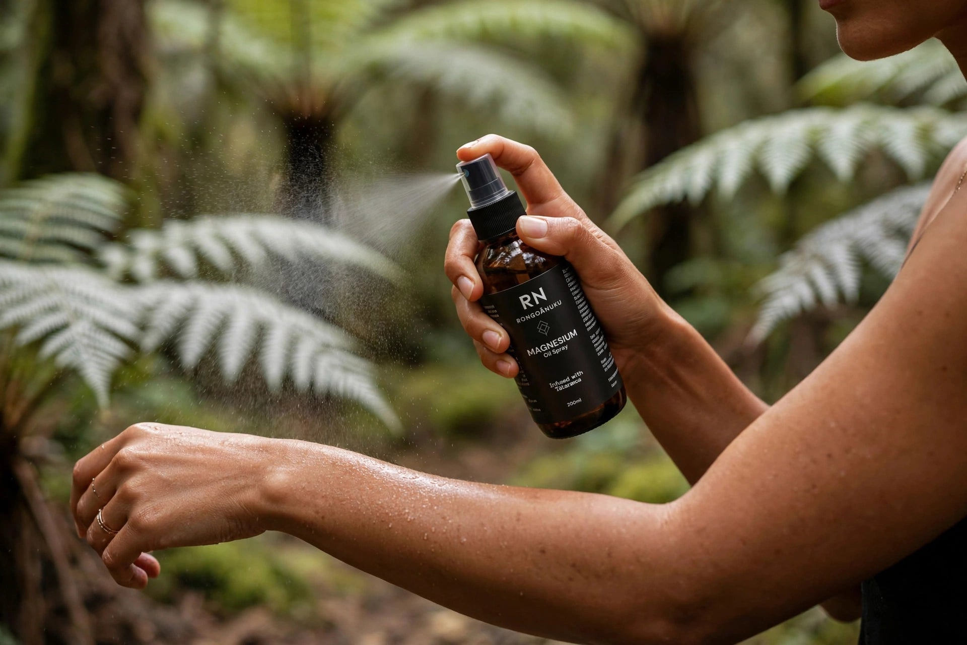 A person outdoors in a lush green native nz forest setting sprays RN magnesium spray onto their skin.